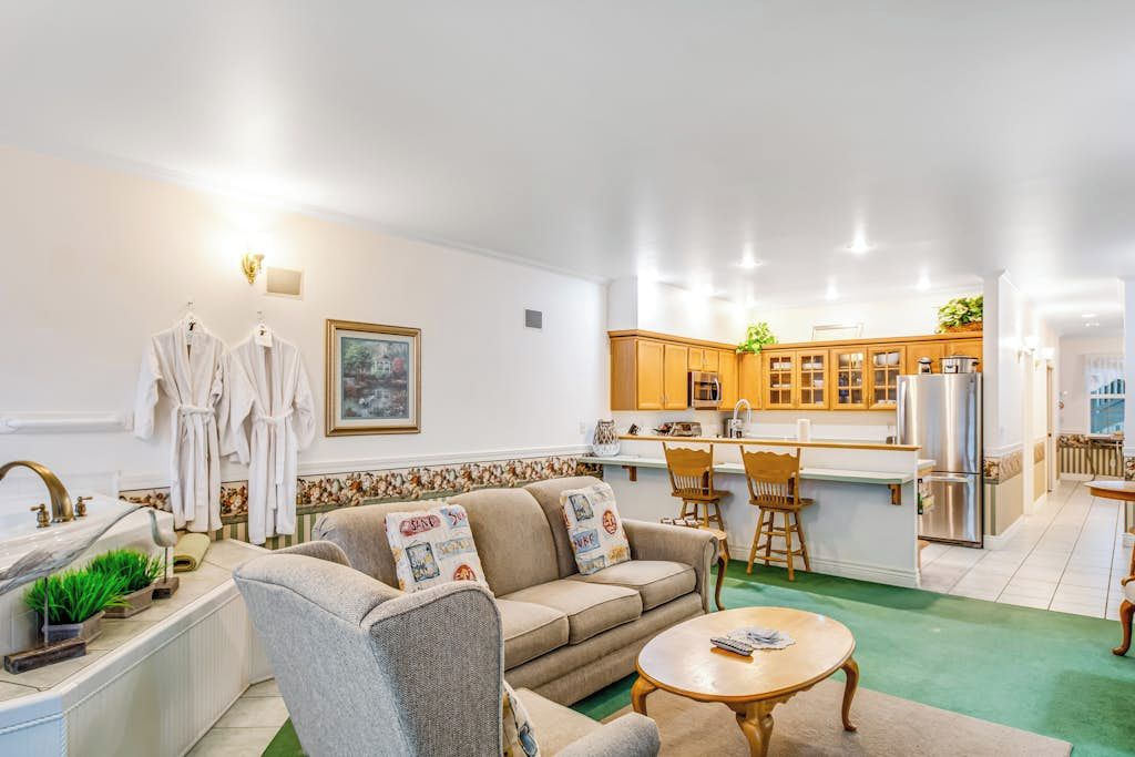 Een woonkamer met een bank, fauteuils, een salontafel en een keuken met houten kasten en een koelkast.