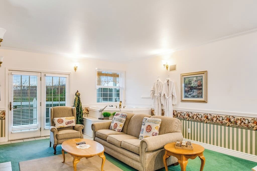 Sala de estar com sofá, poltrona e mesa de centro, janela com persianas e radiador com detalhes decorativos.