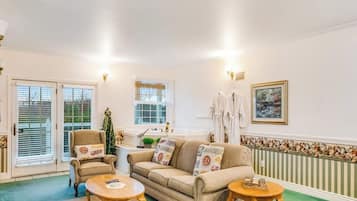 A living room with a sofa, armchair, and coffee table, a window with blinds, and a radiator with a decorative border.