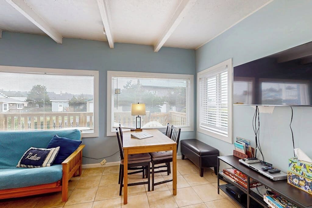 A room with a dining table, a sofa, a bench, and a TV stand with books and a remote control.