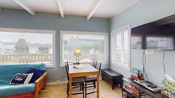 A room with a dining table, a sofa, a bench, and a TV stand with books and a remote control.