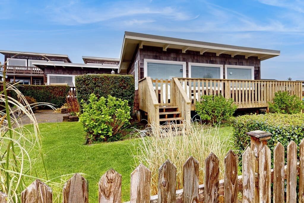 A modern house with a wooden deck, a well-maintained lawn, and a clear sky.