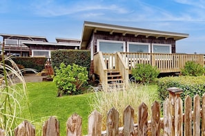 Une maison moderne dotée d’une terrasse en bois, d’une pelouse bien entretenue et surplombant un ciel dégagé.
