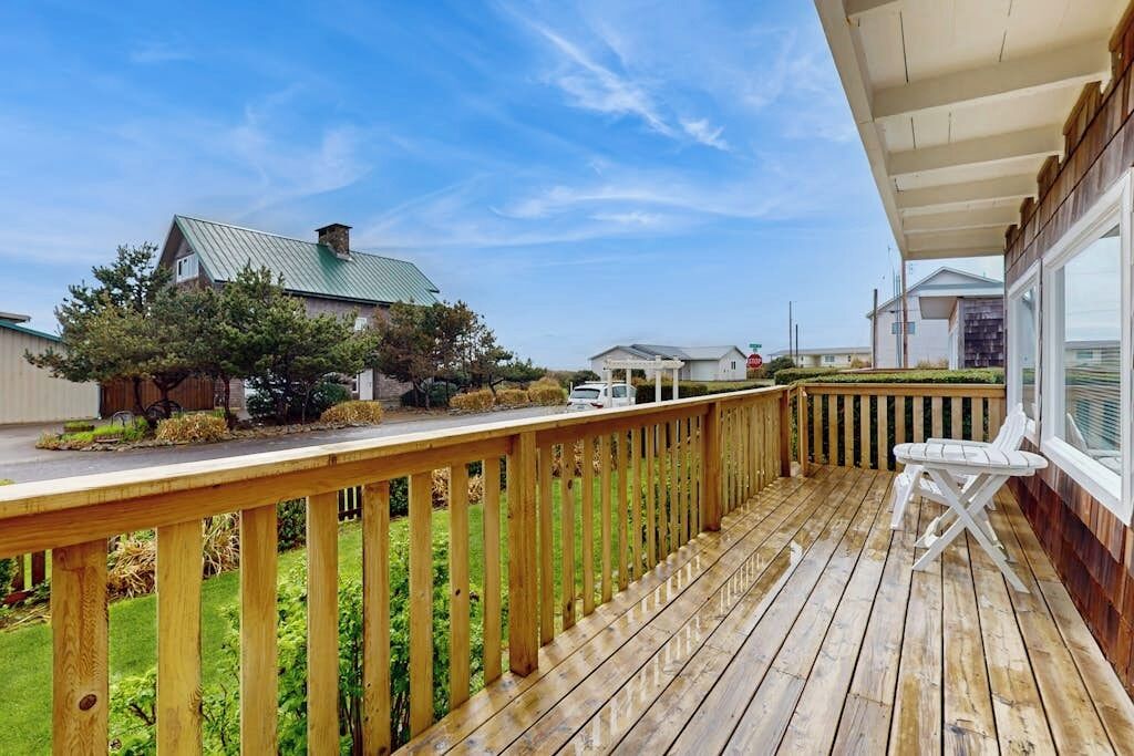 A wooden deck with a white chair, overlooking a grassy area with a house and a barn.