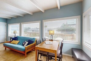 A room with a blue sofa, wooden dining table, and chairs, with large windows and a bench. - Beautiful 1BR Oceanview Dog Friendly (Pacific Beach)