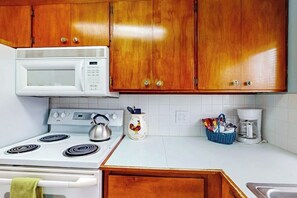 A kitchen with wooden cabinets, a white microwave, a stove, a kettle, and a coffee maker. - Beautiful 1BR Oceanview Dog Friendly (Pacific Beach)