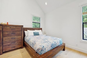 Een slaapkamer met een houten bed, een nachtkastje, een raam en uitzicht op groen.