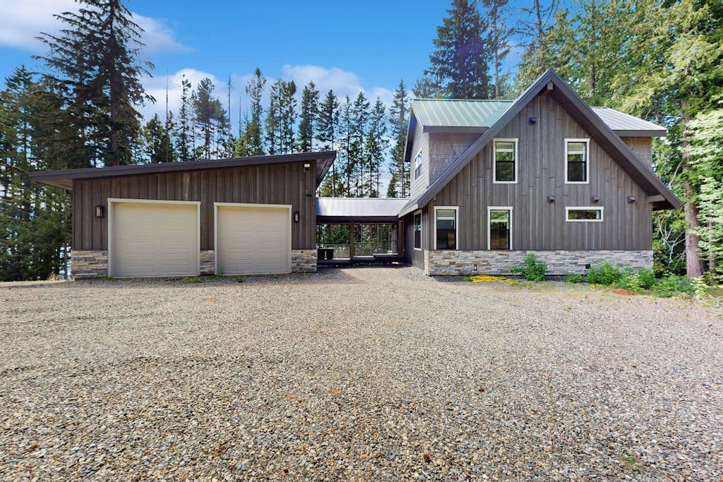 Une maison à deux étages avec une allée en gravier, un garage et des fondations en pierre.