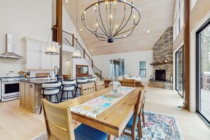 A spacious kitchen with a large island, a dining area with a wooden table, and a stone fireplace. - 4 BR waterfront cabin, dog-friendly (Easton)