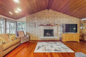 A living room with a brick fireplace, wooden ceiling, and a television. - 3BR Home on the Hood Canal with beach access & views (Poulsbo)