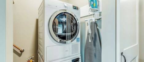 A compact laundry area with a stacked washer and dryer, a fire extinguisher, and a towel rack.