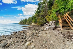 Ein felsiger Strand mit einer Holztreppe, die zu einem bewaldeten Gebiet hinauf führt.