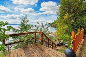 Eine Holzterrasse mit Geländer, die auf ein Gewässer mit umgebender Vegetation blickt.