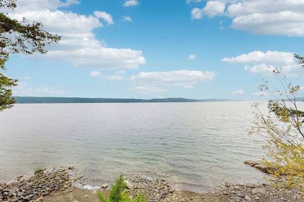 Ein ruhiger See mit steiniger Uferlinie und sanften Hügeln im Hintergrund.