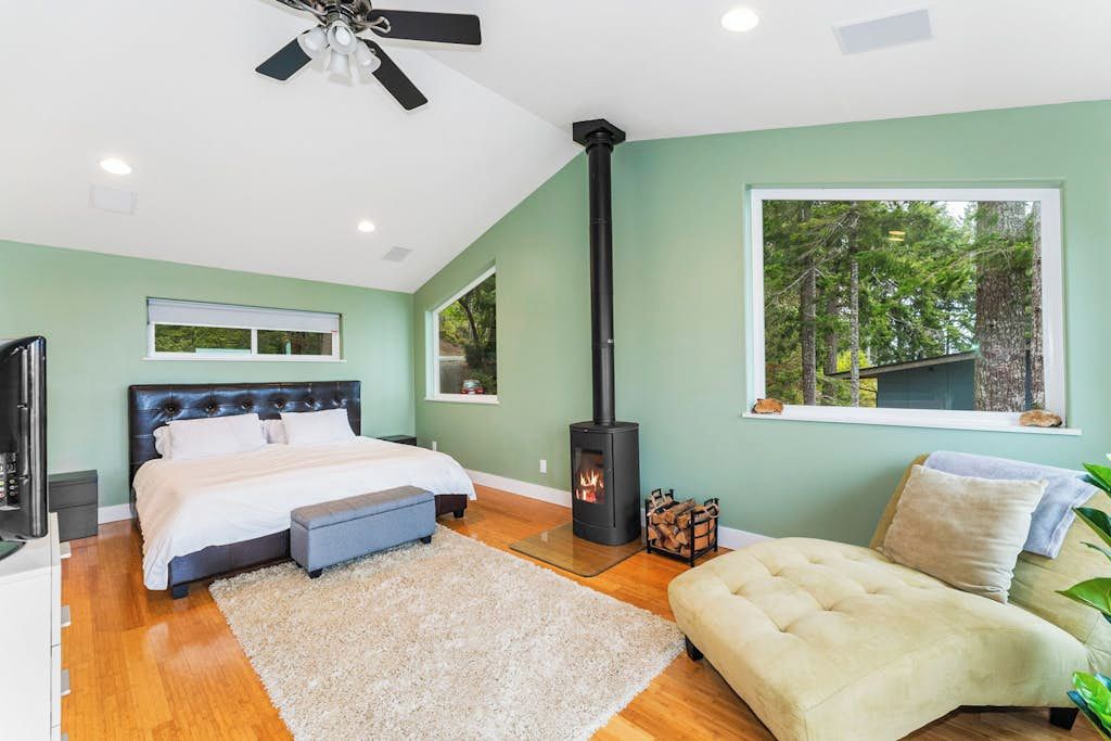 Quarto com cama, sofá, lareira e vista para árvores pela janela.
