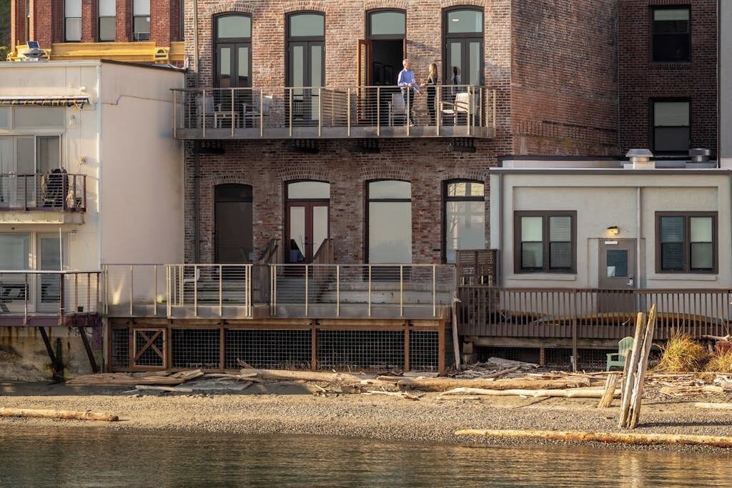 A multi-story building with a balcony, a wooden deck, and a river in the foreground.