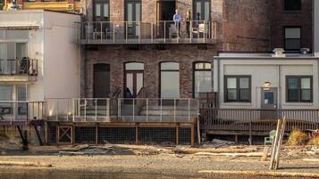 A multi-story building with a balcony, a wooden deck, and a river in the foreground.