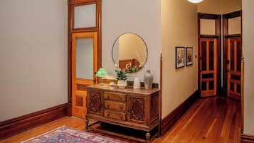 A hallway with a wooden floor, a large mirror, a wooden cabinet, and a patterned rug.