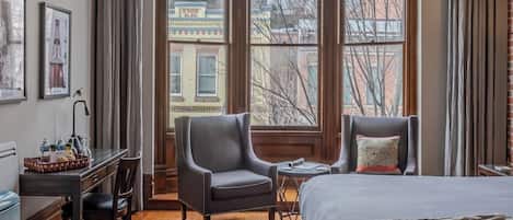 A hotel room with a large window, a bed, a desk, two chairs, and a small table.