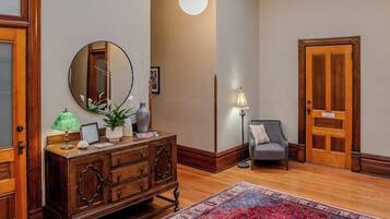A room with a wooden cabinet, a round mirror, a lamp, a chair, and a door.