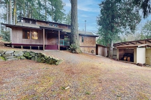 A two-story wooden cabin with a stone foundation, a covered porch, and a garage. - 2 BR cabin with Hood Canal views (Hansville)
