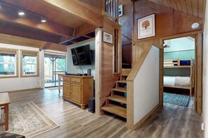 Een houten interieur met een trap, een aan de muur bevestigde televisie en een stapelbed op de achtergrond.