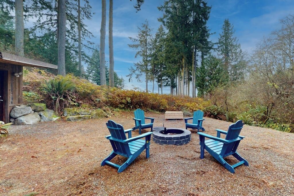 A gravel patio with four Adirondack chairs arranged around a circular fire pit.