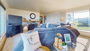 A modern living room with a large TV, comfortable seating, a fireplace, and a view of the outdoors. - 4BR Home with bay and mountain views, beach access (Sequim)