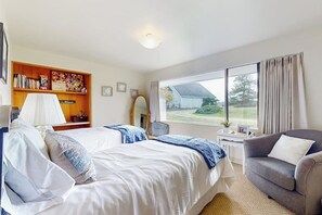 Habitación de hotel con cama, una silla, escritorio, estantería y ventana con vistas al exterior.