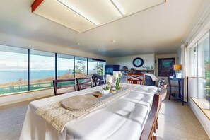 Un comedor con vistas al mar, una mesa redonda con mantel blanco y un ventanal grande.