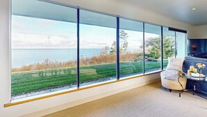 A room with large windows offering a view of a body of water and greenery. - 4BR Home with bay and mountain views, beach access (Sequim)