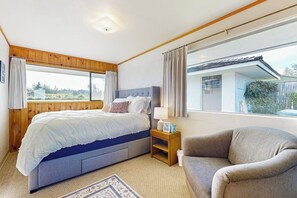 Un dormitorio con cama, mesita de noche, silla y un ventanal con cortinas.