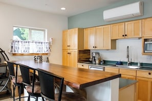 A kitchen with wooden cabinets, a wooden dining table with chairs, a window, and an air conditioning unit. - 1BR lakefront townhouse with dock, 2 kayaks, grill (Port Angeles)