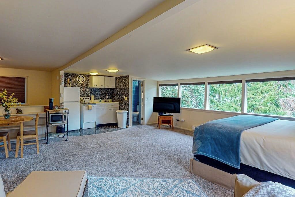 Een kleine kamer met een bed, bureau, kitchenette en televisie.
