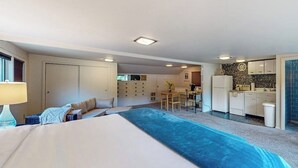 Makuuhuoneessa on suuri sänky, työpöytä ja taustalla pieni keittiönurkkaus.