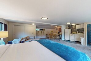 A bedroom with a large bed, a desk, and a kitchenette in the background. - 1BR Bayview Dog Friendly | Patio | Firepit | W/D (Gig Harbor)