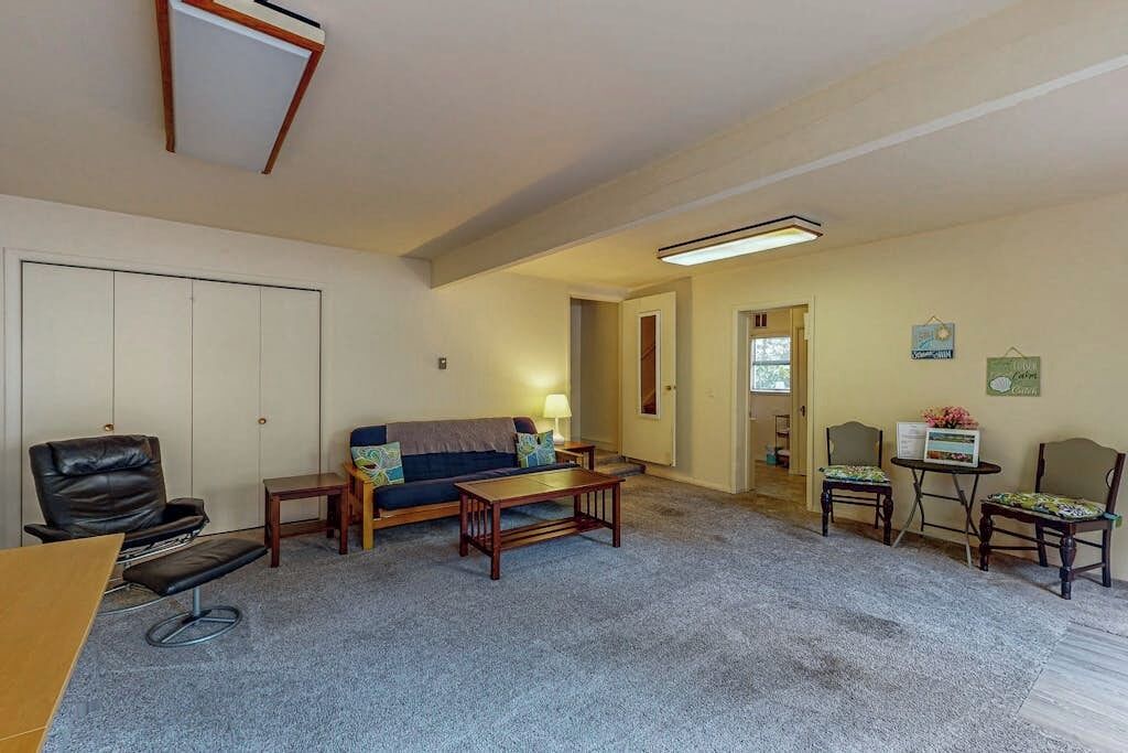 A living room with a sofa, coffee table, and chairs. There is a door leading to another room.