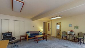 Un salón con sofá, mesa de centro y sillas. Se ve una puerta que da a otra habitación.