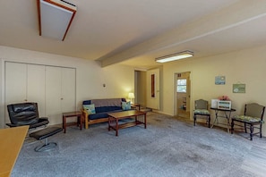 A living room with a sofa, coffee table, and chairs. There is a door leading to another room.