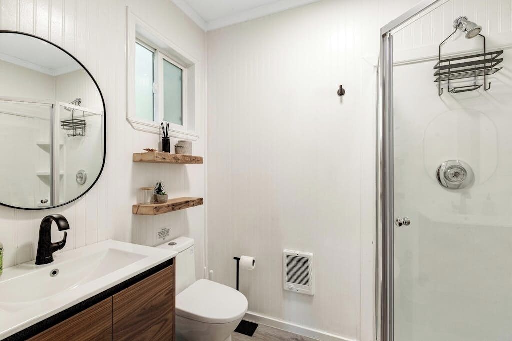 A bathroom with a toilet, sink, mirror, and a glass-enclosed shower.