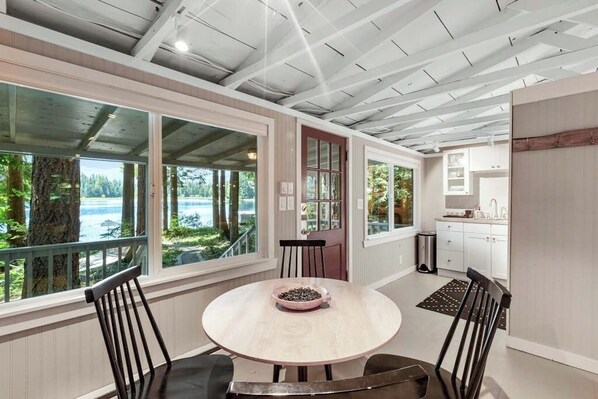 A dining area with a round table, chairs, and a view of the outdoors. - Luxe Studio Lakefront | Dock | Deck | Firepit (Fall City)