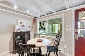 A dining area with a round table, four chairs, a cabinet, and a window with a view of greenery. - Luxe Studio Lakefront | Dock | Deck | Firepit (Fall City)