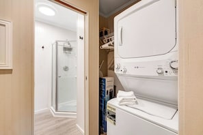 A laundry room with a front-loading washer and dryer, a glass shower enclosure, and a storage area with shelves. - Luxe Studio Lakefront | Dock | Deck | Firepit (Fall City)