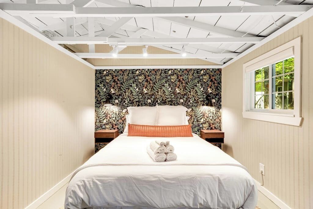 A bedroom with a bed, a window, and a patterned wallpaper.