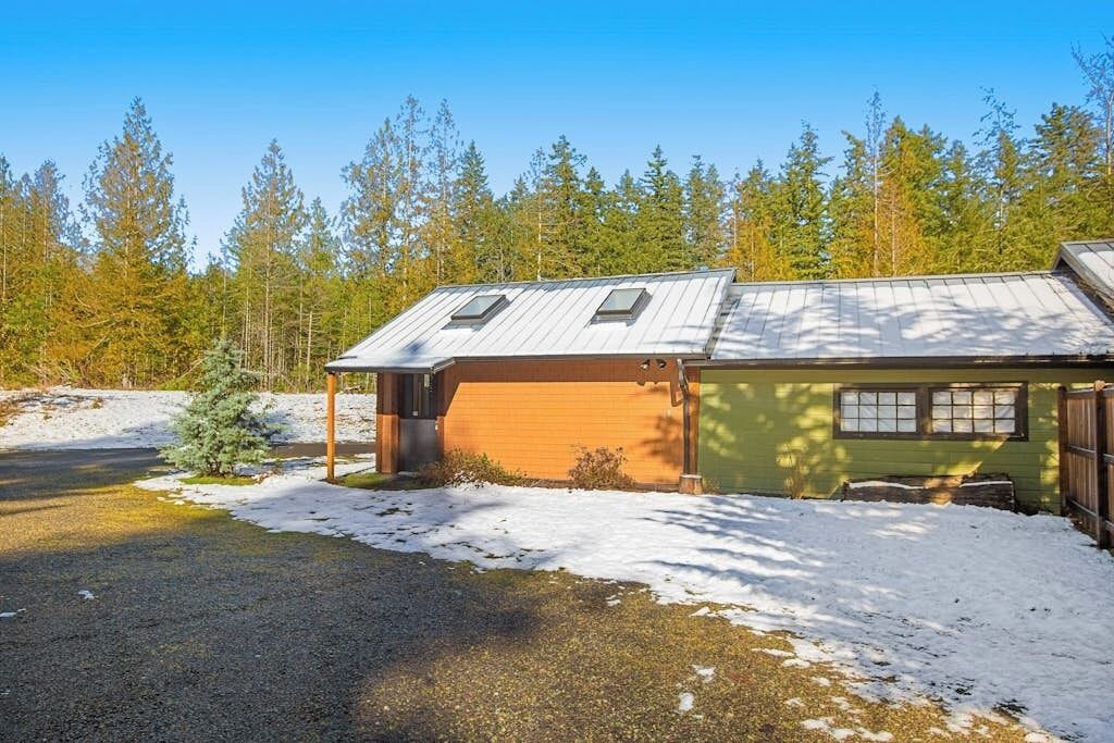 En toetagers bygning med garage og en overdækket veranda, omgivet af et sneklædt landskab og tæt skov.