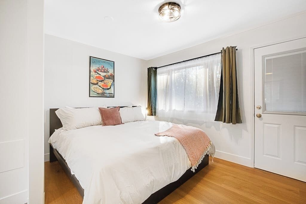 Une chambre à coucher avec un lit, une porte, une fenêtre avec des rideaux et un tableau accroché au mur.