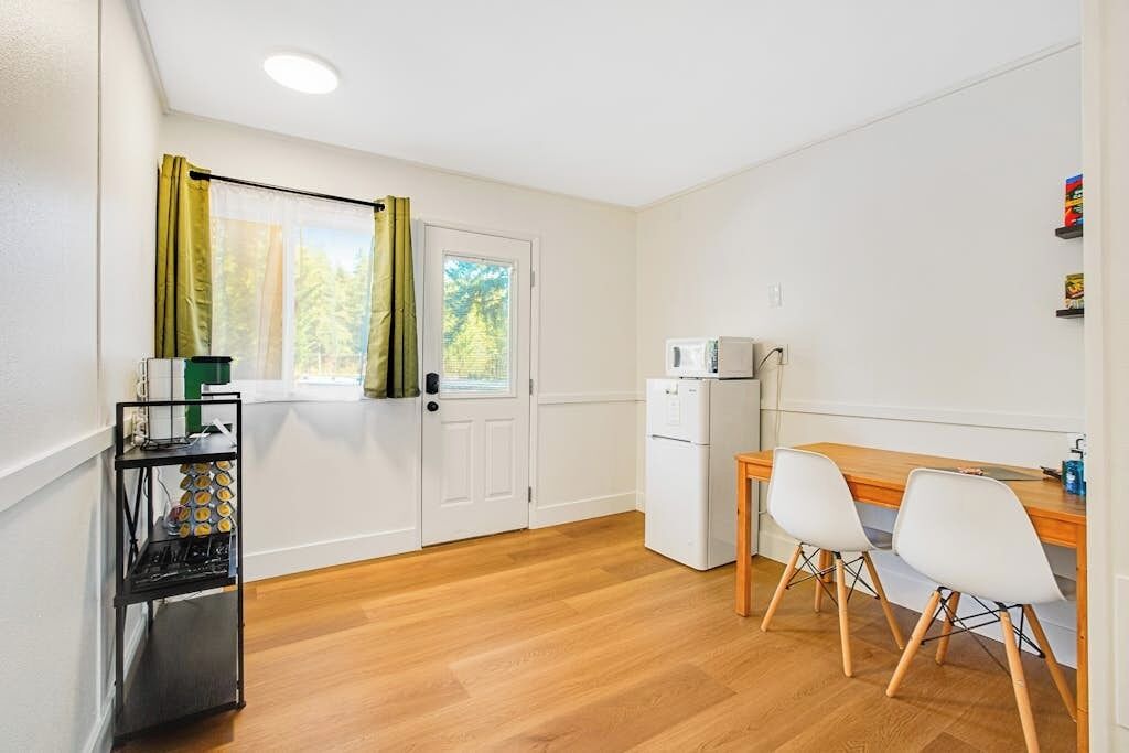 Una cocina compacta con microondas, un refrigerador pequeño y una mesa de madera con dos sillas.