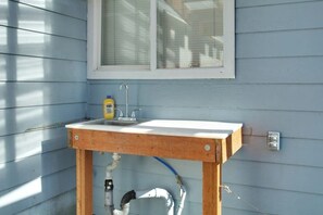 Een klein buitenkeuken met een spoelbak, houten tafel en een raam erboven.