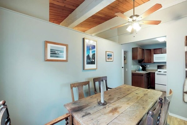 Een eethoek met een houten tafel en stoelen, een plafondventilator en ingekaderde foto's aan de muur.