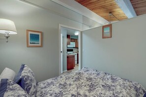 A bedroom with a bed, a nightstand, a lamp, and a door leading to a kitchen. - Incredible 2BR Bayview 1st-Floor (Westport)